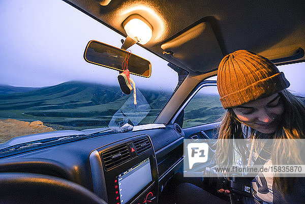 Frau mit Kamera und Hut sitzt im Auto und schaut auf den Sonnenuntergang