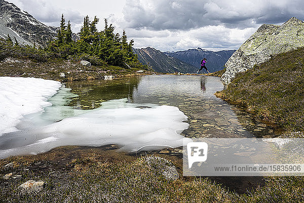 A women jumps over water on the edge of an alpine pool on summer day in the mountains of British Columbia.