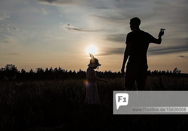 Silhouette eines Vaters und einer Tochter  die draußen bei Sonnenuntergang zusammen spielen