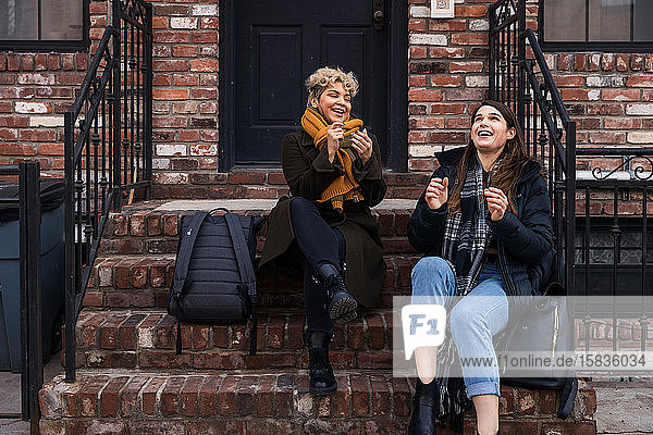 Glückliche Freundinnen unterhalten sich  während sie im Winter auf den Stufen in der Stadt sitzen