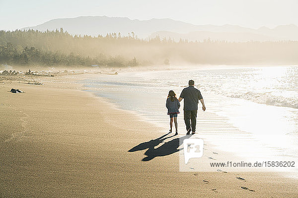 Vater und Tochter spazieren bei Sonnenuntergang am Strand entlang
