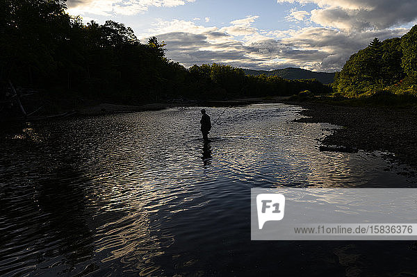 Ein Fischer watet bei Sonnenuntergang in einem Fluss