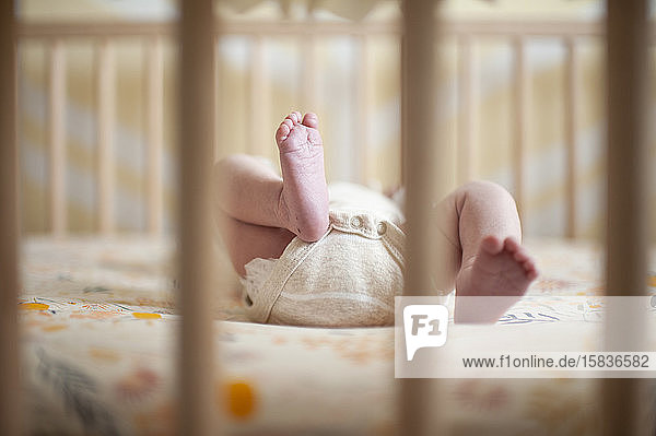 Neugeborene Mädchenfüße durch das Kinderbett zu Hause