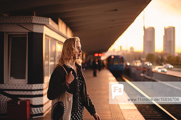 Thoughtful young woman waiting for train at subway station at sunset
