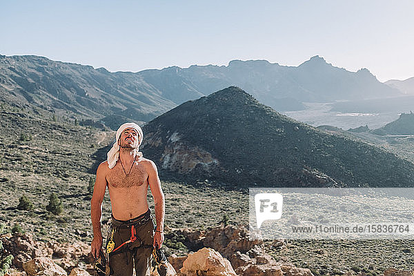 A shirtless climber stands on rock with mountain in background