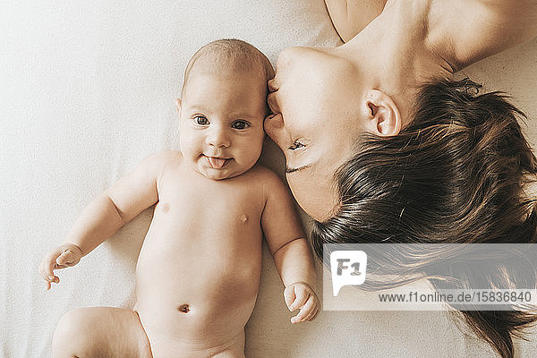 Mutter und neugeborener Sohn liegen ausgestreckt im Bett  Mutter küsst ihren Sohn.das neugeborene Kind streckt die Zunge heraus