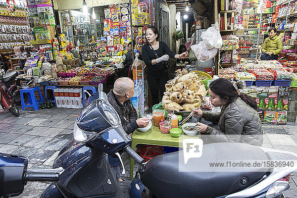 Ein Ehepaar isst auf dem Bürgersteig in Hanoi  Vietnam  Straßenessen.