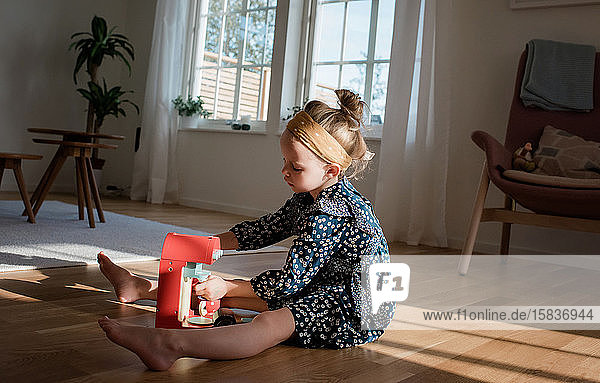 Ein junges Mädchen spielt mit einem vorgetäuschten Kaffeeservice zu Hause im Fensterlicht