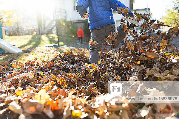 Kind tritt im Herbst ein Bein in einen Laubhaufen draußen im Hof
