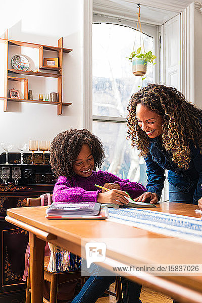 Lächelnde Mutter hilft Tochter bei den Hausaufgaben bei Tisch im Wohnzimmer