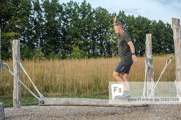 Ein Mann balanciert auf Schwingbalken im Hindernisparcours im baumbestandenen Park