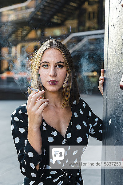 Elegant trendy woman exhaling smoke from cigar looking at camera
