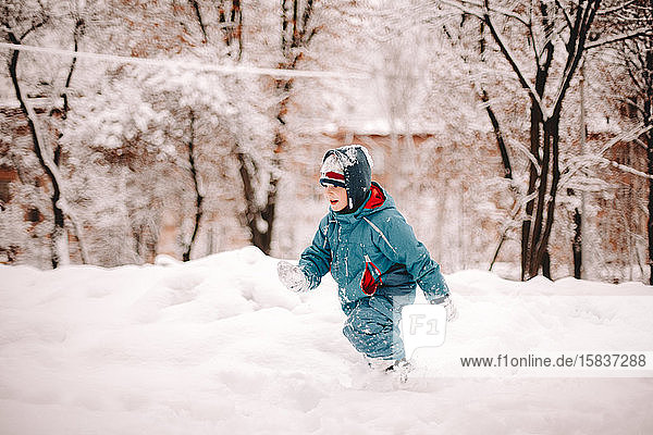 Boy running in snow covered field in park in winter