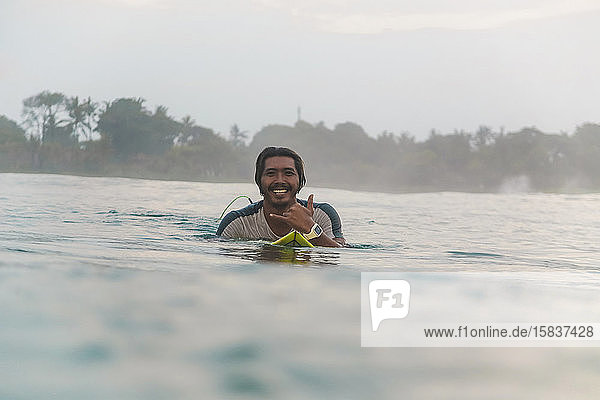 Porträt eines glücklichen Mannes  der auf einem Surfbrett auf dem Meer liegt