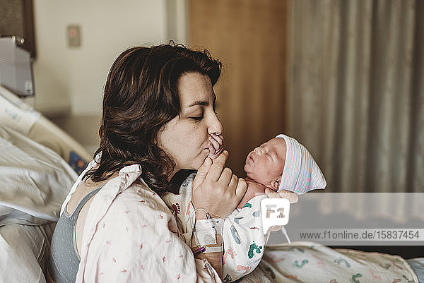 Neue Mutter im Krankenhaus küsst neugeborenen Sohn Hand