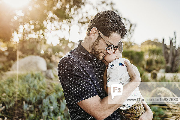Portrait of father embracing young toddler son with sun behind them