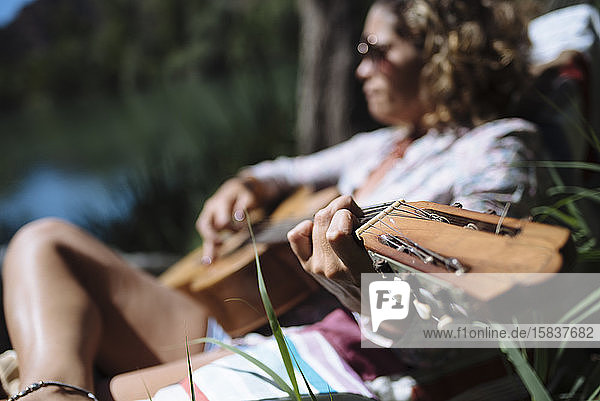 Frau mit Sonnenbrille  die Gitarre spielt und auf einer Hängematte liegt.