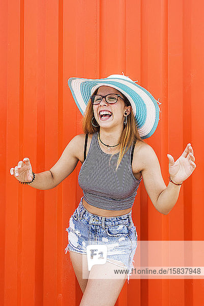 Foto einer hübschen Frau mit Hut  die gegen eine orangefarbene Wand lacht