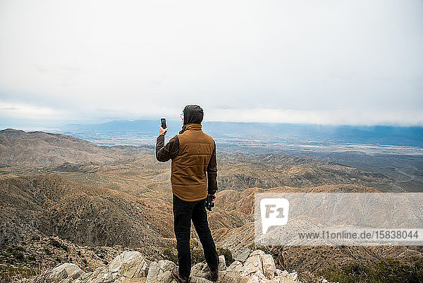Mann benutzt Telefon auf einem Hügel mit Wüstentälern unter grauem Himmel