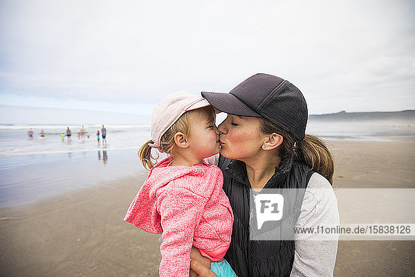 Mutter gibt ihrer Tochter am Strand einen dicken Kuss.