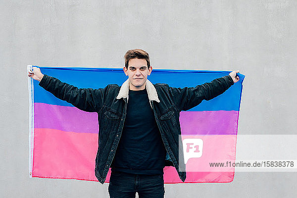 Junger Mann mit der Flagge der Bisexuellen auf grauem Hintergrund