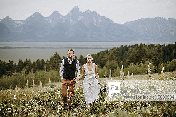 happy smiling newlyweds walk through field of wildflowers in Tetons