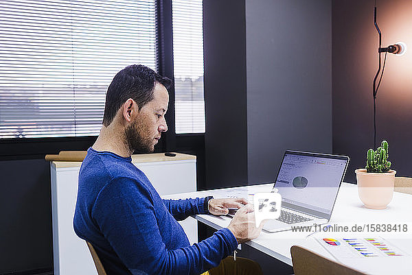 Young businessman reading his smartphone. Portrait of business man reading message with smartphone in office. Man working at his desk at office.