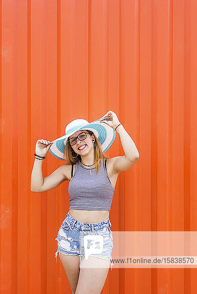 Foto einer hübschen Frau mit Hut  die gegen eine orangefarbene Wand lacht