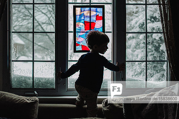 Ein kleiner Junge steht vor einem verschneiten Fenster.