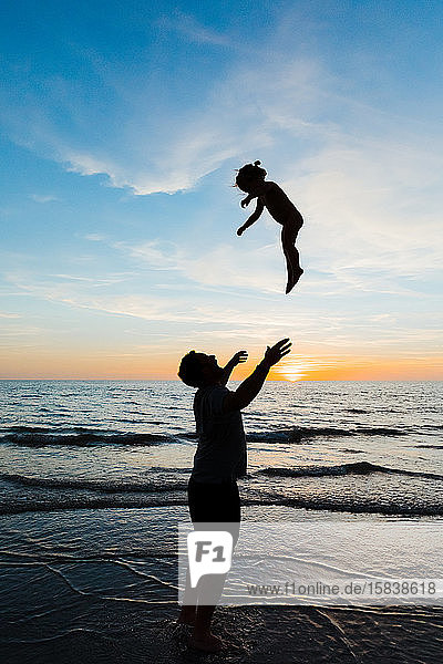 dad throws his toddler daughter into the air at florida beach sunset