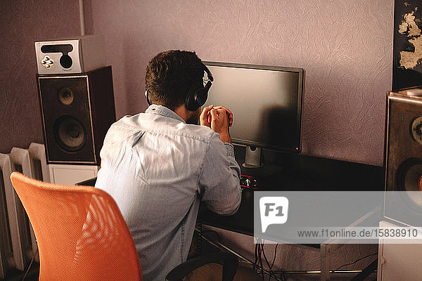 Konzentrierter Mann mit Kopfhörern am Desktop-Computer sitzend