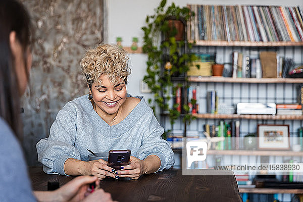 Lächelnde Frau sendet Textnachrichten auf einem Smartphone  während sie mit einem Freund zu Hause sitzt