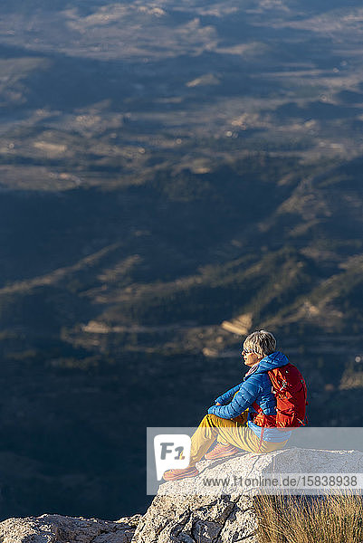 Young woman standing on rocks on top of a mountain looking over.
