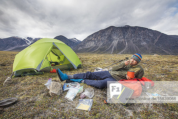 Climber eats meal  relaxes  charges devices at campsite.