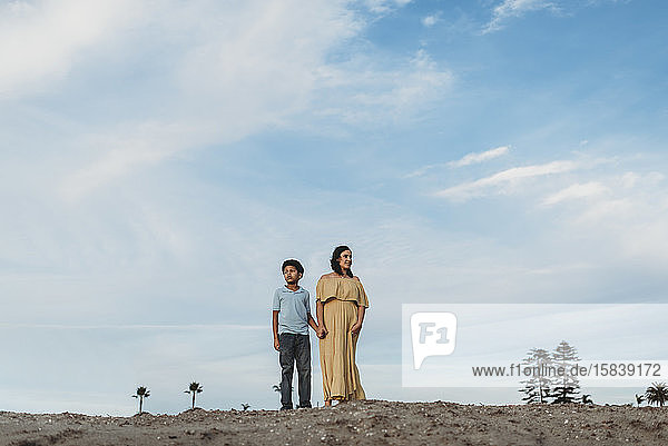 Junge Mutter und schulpflichtiger Sohn stehen auf Stranddüne