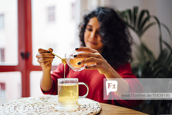 Brünette Frau versüßt einen Tee mit Honig