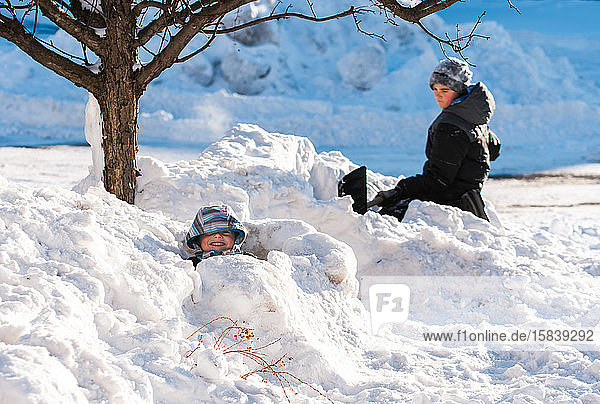 Two boys building snow forts with shovels on a sunny winter day.