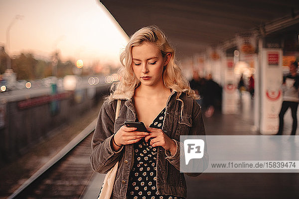 Junge Frau wartet am U-Bahnhof mit einem Smartphone auf den Zug