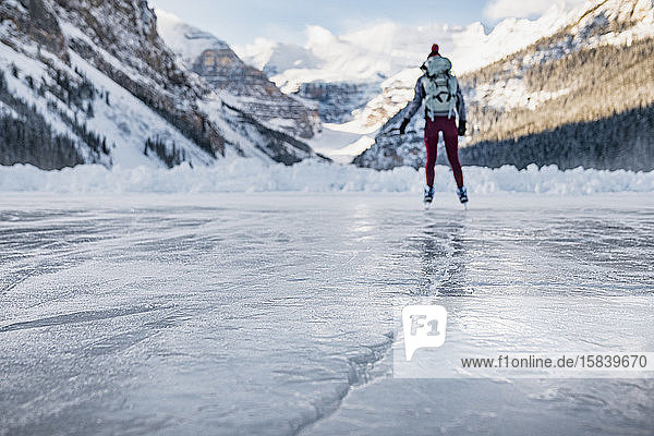 Junge Frau beim Schlittschuhlaufen auf dem gefrorenen Lake Louise in Banff Towards Mountains