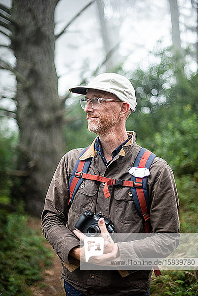 Porträt eines Fotografen mit Hut haltender Kamera im Wald