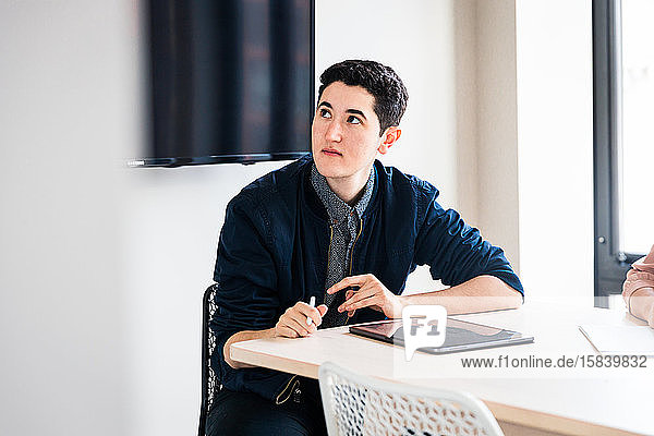 Junger Geschäftsmann konzentriert am Tisch sitzend bei Besprechung im Büro