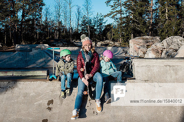 Mama sitzt mit ihren Kindern auf einem Skatepark im Freien und amüsiert sich