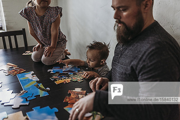 Familie mit kleinen Kindern vervollständigt Puzzle zu Hause während der Isolation
