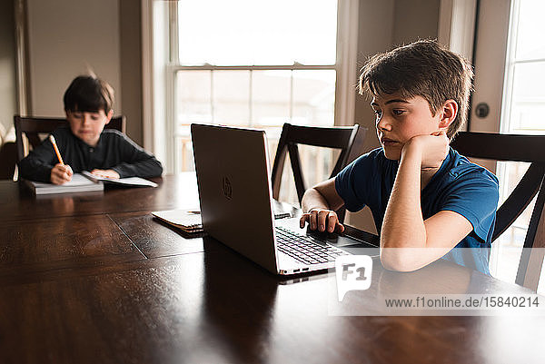 Jungen  die zu Hause mit einem Laptop an ihren Hausaufgaben arbeiten  pendeln nach Hause.