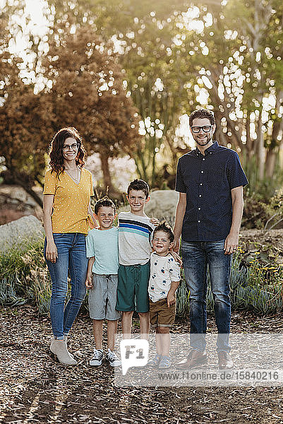 Porträt einer Familie  die im sonnigen Kaktusgarten vor der Kamera lächelt