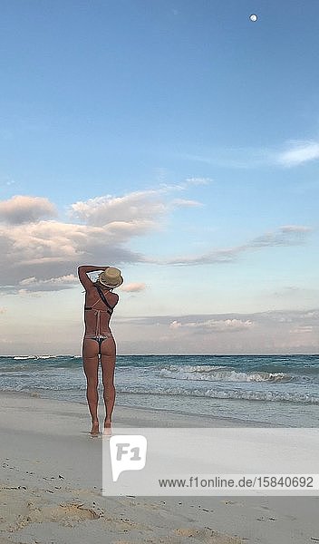 Frau von hinten am Strand im Badeanzug beim Fotografieren des Sonnenuntergangs