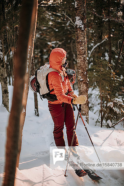 Backcountry-Skifahrerin blickt auf die aufgehende Sonne am kalten Morgen im Wald