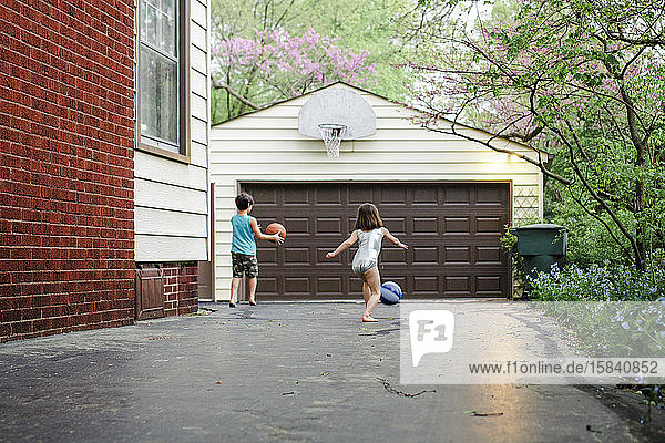 Zwei kleine Kinder spielen in der Dämmerung in der Einfahrt gemeinsam Basketball