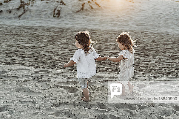 Seitenansicht von jungen Kleinkind-Mädchen  die sich an den Händen halten und am Strand spazieren