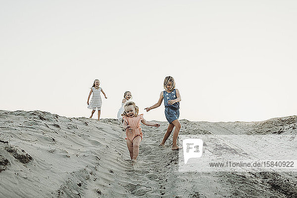 Vier junge Schwestern laufen bei Sonnenuntergang am Strand im Sand